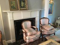 Two carved wood accent chairs with plaid upholstery positioned before a fireplace with matching ottoman visible