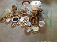 Wide view showing assorted china pieces including plates, bowls, cups, vase, and glassware arranged on floor.