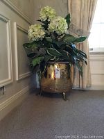 Overall view of artificial hydrangea arrangement in brass planter against wall and drape