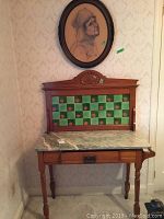 Front view of wooden table with marble top, decorative tiled back panel and carved detail at the top center.