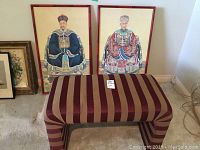 Two framed Asian portrait prints in traditional attire leaning against wall behind a striped bench.