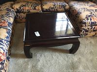 Square dark wood coffee table with curved legs on carpet.