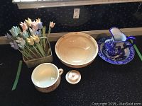 Wooden tulips in basket, ceramic bowl, larger bowl, lid, and blue and white jug with plate arranged on black surface.