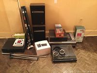 Full view of all items in the lot arranged on floor against wall, showing stereo equipment, speakers, violin case, tripod, and various boxed items.
