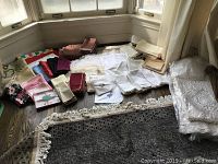 Overview of assorted linens spread on floor including folded tablecloths and napkins in various colors and styles next to rug