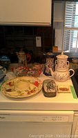 Wide view of lot with four teapots, serving dish, and trinket box arranged on kitchen counter.