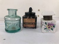 Front view of all three inkwells showing the blue Underwoods jar, black Carter's ink bottle, and white china floral inkwell.