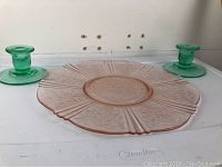 Pink Depression glass cake plate with floral and linear design. Plate is large and round with a central circular area. Visible scratch and felt attached.