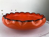 Full view of bright orange art glass bowl with black scalloped rim