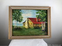 Full view of the framed painting depicting a cottage with a red roof, trees, and a grassy foreground, with a partly cloudy blue sky.