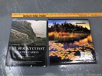 Two hardcover books side by side with a ruler for size reference. Left book titled 'The Rocky Coast' by Rachel Carson. Right book titled with scenic Canadian image cover; contains stamp collection.