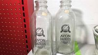 Two clear glass milk bottles with Avon Dairies Limited logo side-by-side