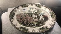 Oval platter showing full village design with trees, houses, church, water, and floral border.