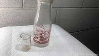 Glass milk bottle with red lithograph child on swing and advertising text 'Swing to MILK The UNIVERSAL FOOD', along with a small clear glass creamer.