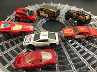 Seven vintage toy cars displayed on a circular clear plastic stand, showing varied models and colors