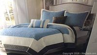 Full view of the made-up bed showing the blue, cream, and brown striped queen size coverlet with two matching pillow shams and decorative pillows.