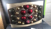 Photo of boxed set of 24 glass Christmas ornaments in gold and red colors, assorted sizes.