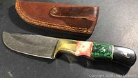 Knife with blade partially exposed showing Damascus steel pattern and part of leather sheath