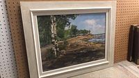 Framed oil painting showing landscape with birch trees and water on a sunny day.