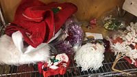Photo showing vintage red Christmas tree skirt and multiple Santa Claus face decorations with yarn beards, some white flower arrangements and red decorative items.