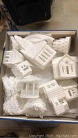 Box containing a collection of white crochet Christmas houses in various shapes including rectangular and pitched roofs.