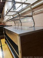 Side angle showing stainless steel countertop and sneeze guard above with support frame