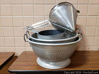 Stacked aluminum colanders and flour sifter showing perforations and handles