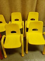 Front view of six yellow preschool chairs arranged in two rows, showing molded plastic seats and backs with cut-out handles, and tubular metal legs and armrests.