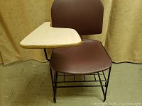 Front angle view of school desk showing brown seat and backrest, black metal frame and attached wooden desktop.