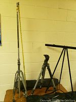 Wide view of three stands: two metallic camera stands and one black collapsible musical stand, with cases visible behind them.