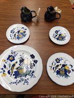 Photo showing four Spode ceramic plates with blue and yellow floral and basket pattern along with two dark-glazed pitchers featuring moose handles, all placed on a wood surface.