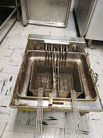 Top view of GE stainless steel commercial deep fryer with two wire fry baskets inside, control panel with knob and power indicator light visible. Shows signs of heavy use with oil stains.