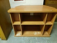 Front view of wooden TV console showing cubbies and storage areas with wear marks on bottom shelf.
