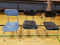 Three metal framed chairs in a gym or hall environment—one blue and two black.