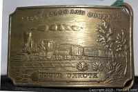 Close-up of front side of brass belt buckle with embossed Wells Fargo and Company train and South Dakota text.