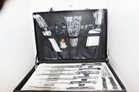 Open briefcase showing 12 pink-handled kitchen knives and utensils covered in protective plastic sheathes and wraps.