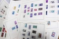 Photo showing multiple white album pages spread out with a variety of colorful postage stamps dated from the 1940s-1980s mounted neatly.