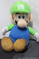 Front view of the Luigi plush toy showing the full body, green hat with 'L' logo, blue overalls, green shirt, white gloves, and brown shoes.