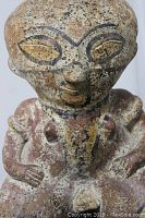 Front view of the ceramic Toltec figure showing head, face markings, torso, and arms positioned on hips.