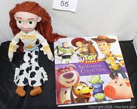 Front view of Jessie plush doll sitting next to the Toy Story hardcover storybook collection with colorful character illustrations on the cover.