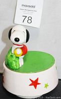 Side view of the Snoopy musical spinning figurine showing Snoopy seated atop the base with star decorations.