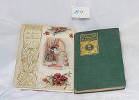 Two antique books displayed side by side, one green with gold embossed title, other with decorated illustrated cover with flowers and a woman at a door