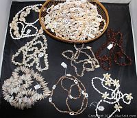 Top-down view of a woven basket filled with various styles of vintage seashell necklaces arranged on a black surface, showing detail and diversity in shells and colors.