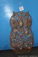 Front view of wire owl sculpture lit with small lights against a blue background, showing intricate wire detailing and overall shape.