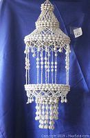 Front view of the vintage decorative hanging white seashell flower/plant holder against a blue background to show overall structure and size.