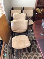 7 wood frame dining chairs with beige fabric seats and backs arranged closely together, showing general condition and design.
