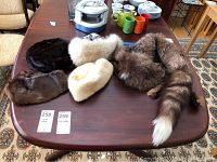 All five fur hats and one fur stole arranged on a wooden table, showing their colors and sizes.