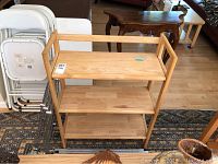 Wooden three-tier folding storage shelf, light natural color, visible shelving and frame intact with minor scratches.