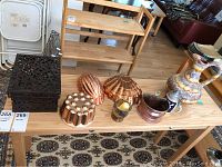 Table displaying assorted decorative items including a large ceramic pitcher, stein, copper plant holder, three tin wall hangings, a metal container with bird etchings, and other copper mold pieces.