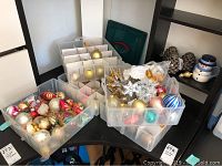 Two translucent plastic storage bins filled with assorted glass holiday ornaments including gold, red, striped, vintage baubles and decorative pieces such as snowflakes and gold leaves.
